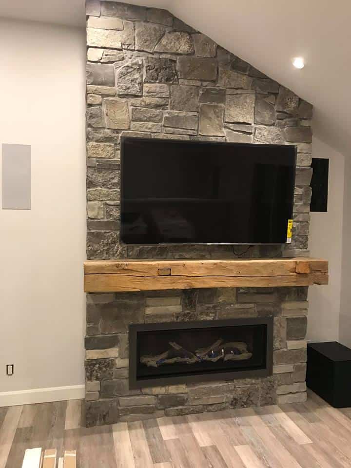 Enviro c44 linear fireplace with driftwood, natural stone veneer wall with tv mounted and rustic beam mantel