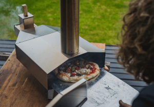 Safe home fireplace person cooking pizza in pizza oven on backyard deck pizza oven benefits blog image on safe home fireplace website